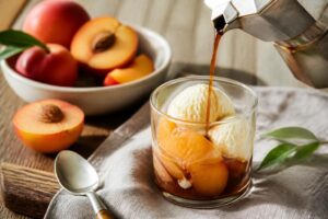 Affogato alla pesca con gelato alla vaniglia servito in un bicchiere trasparente, con pezzetti di pesca fresca e succo di frutta, dessert estivo italiano
