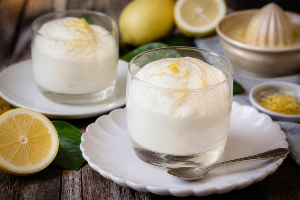 Mousse al limone senza panna e senza uova servita in bicchierini di vetro con scorza grattugiata e foglie di menta fresca