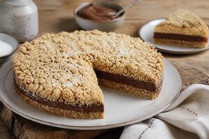 Sbriciolata fredda alla Nutella e cocco senza forno, tagliata a fetta per mostrare gli strati: base di biscotti al cacao, crema al mascarpone e cocco, copertura alla Nutella