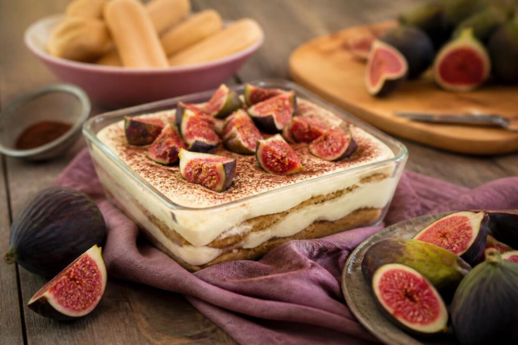 Tiramisù ai fichi senza uova in coppetta trasparente con strati di crema al mascarpone, savoiardi e fichi freschi a fette, su sfondo di lino chiaro