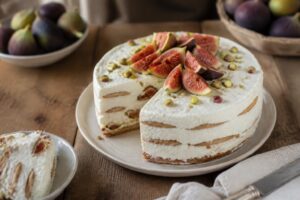 Torta fredda ricotta e fichi senza uova, decorata con fichi freschi tagliati a ventaglio, miele di acacia e pistacchi tritati, su piatto bianco